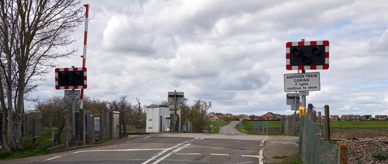 The level crossing has single Barriers with village of Eastrea in the background