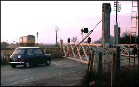 A Mini waits at the crossing gates next to Whittlesea station